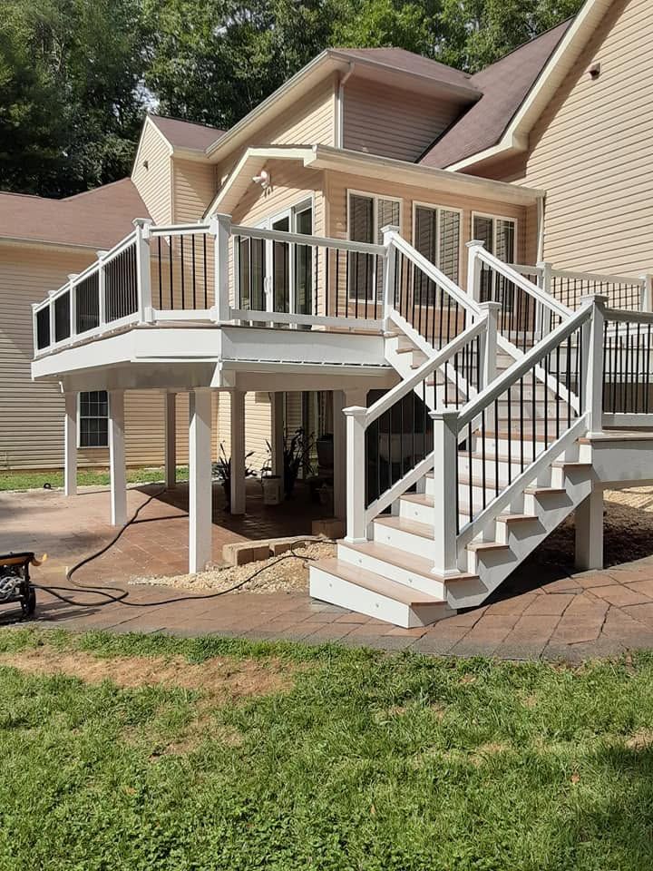 White backyard deck with stairs, railing, and support posts attached to a tan house, under construction