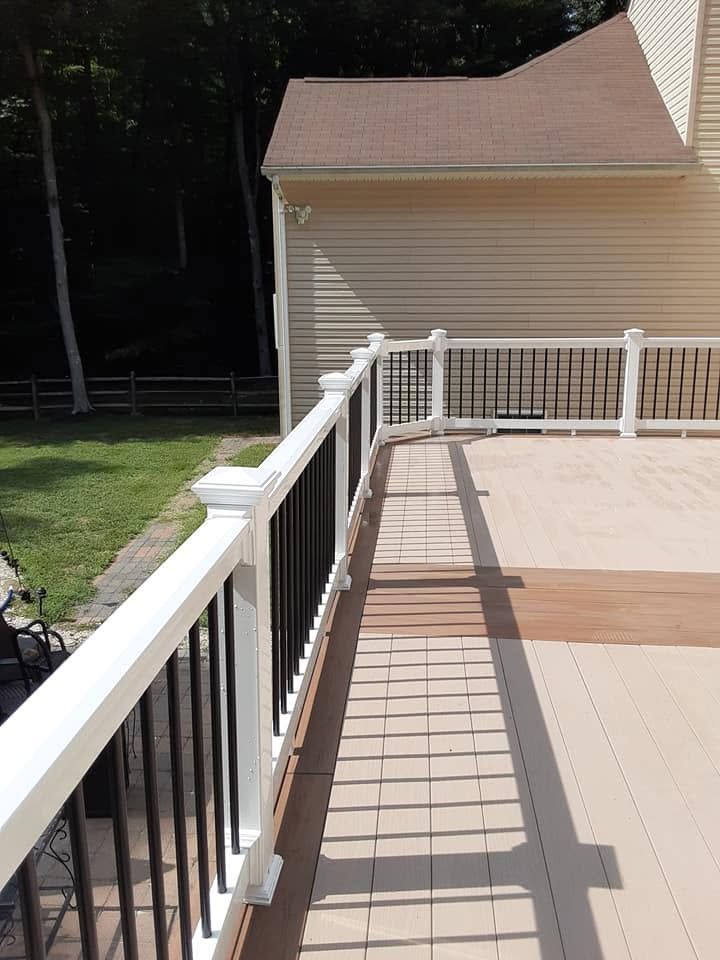 Deck with white railing beside a tan house and grassy yard in sunlight