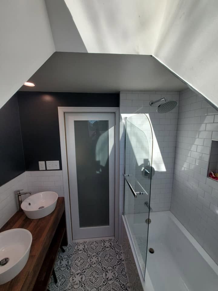 Modern bathroom with double sink vanity, glass shower, and skylight under a sloped ceiling