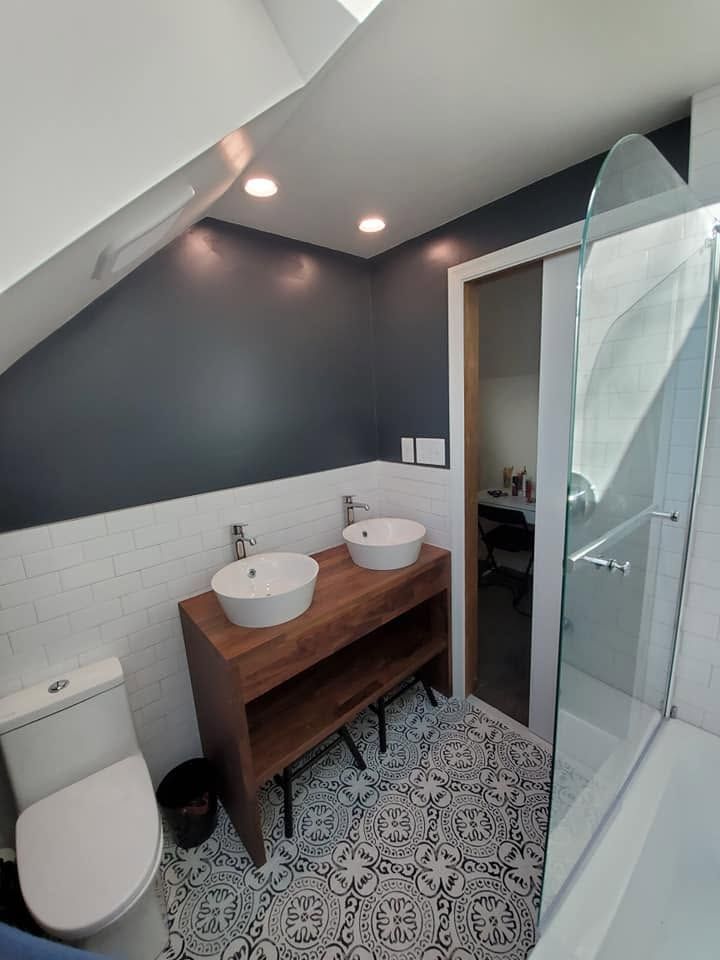 Modern bathroom with sloped ceiling, patterned floor, wood vanity, twin sinks, and toilet