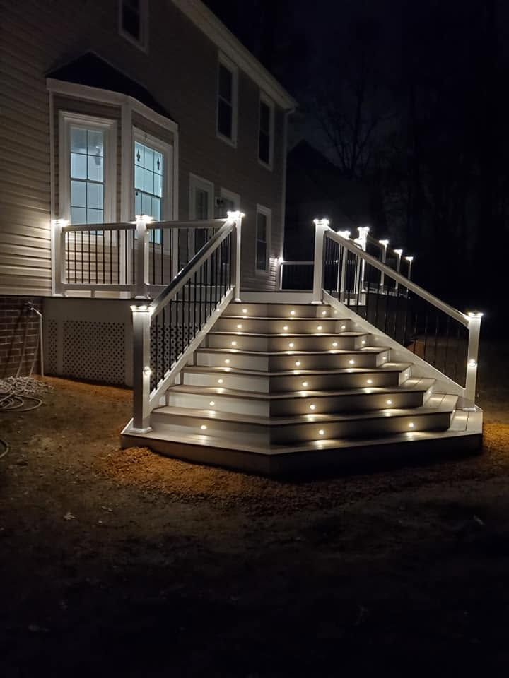 Nighttime exterior of a house with illuminated wooden stairs, railings, and porch lights