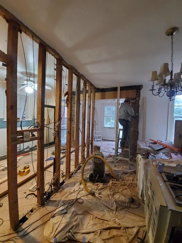 Renovation in progress inside a gutted room with exposed framing, debris, and tools on the floor.