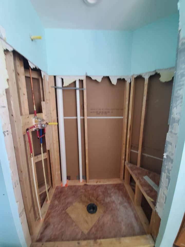 Partially renovated bathroom with exposed studs, blue walls, and a tiled floor with a drain.