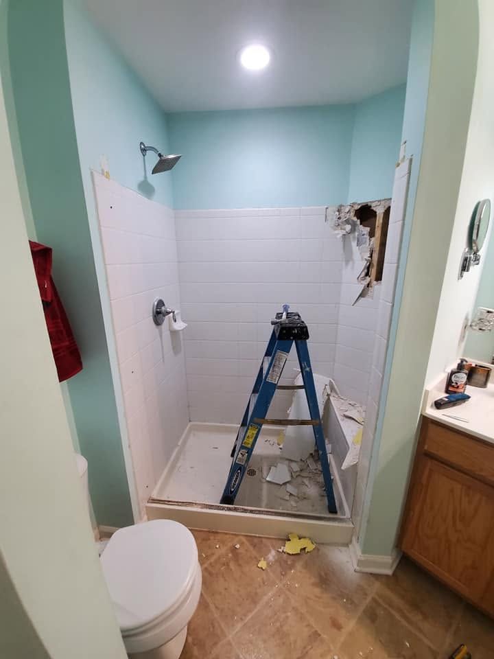 Bathroom under renovation with ladder in a shower stall, white tile walls, and light blue paint.
