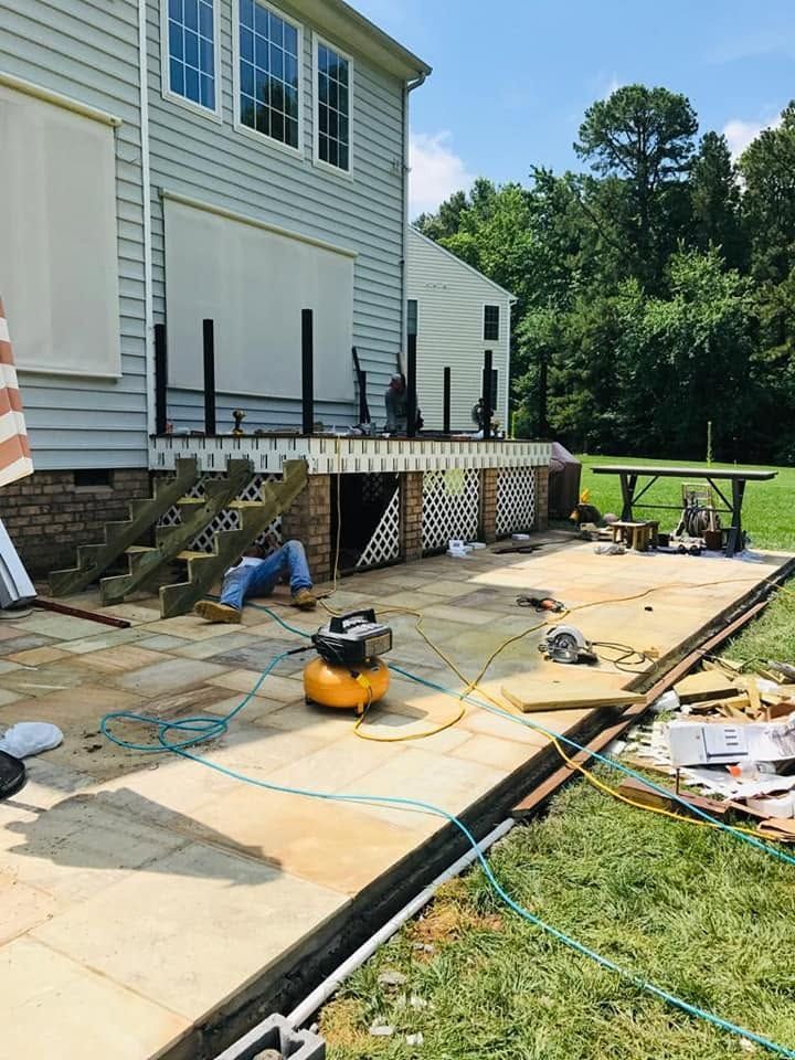 Back patio construction with exposed framing, tools, and unfinished concrete walkway beside a white house