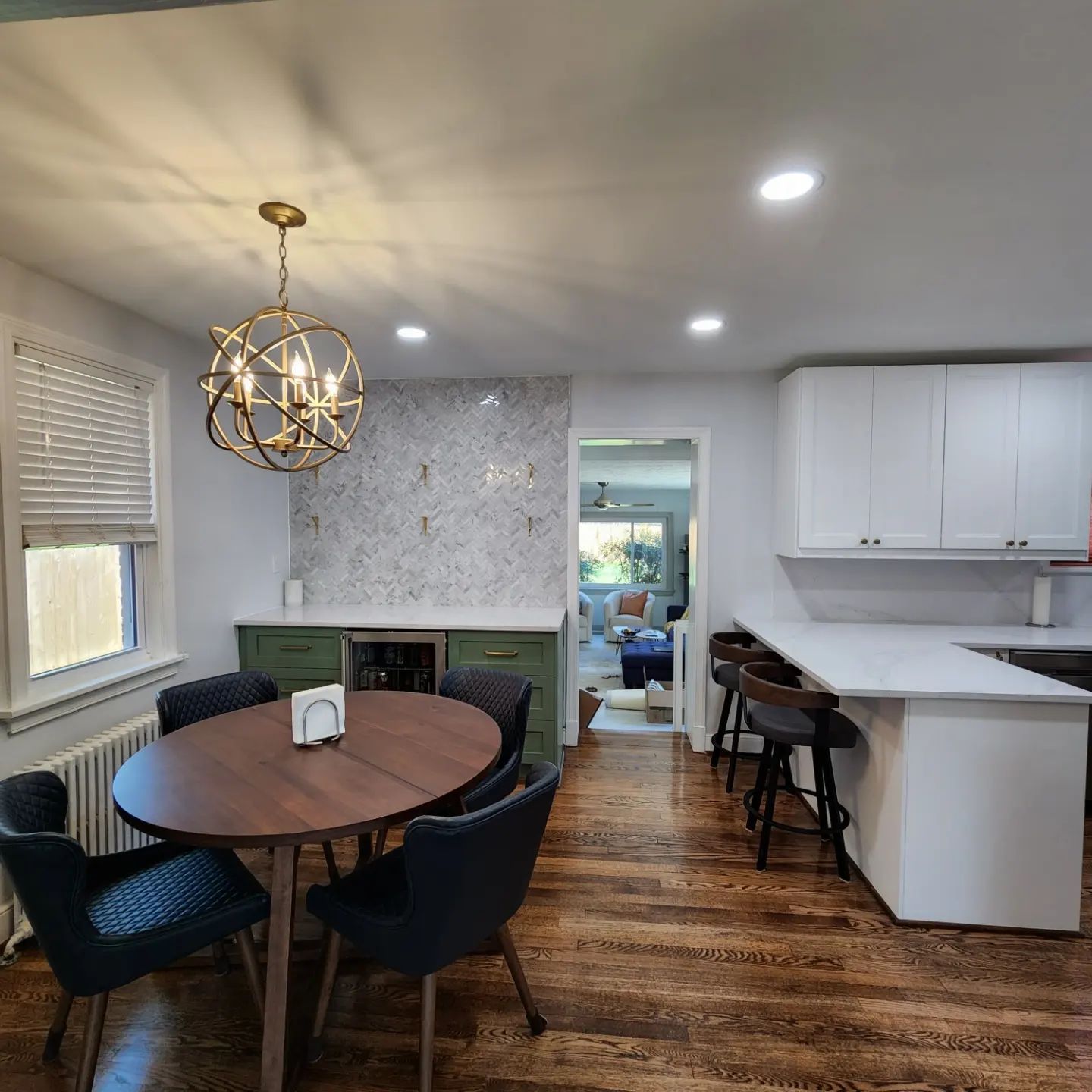 Open kitchen and dining area with round table, black chairs, white cabinets, and hardwood floors
