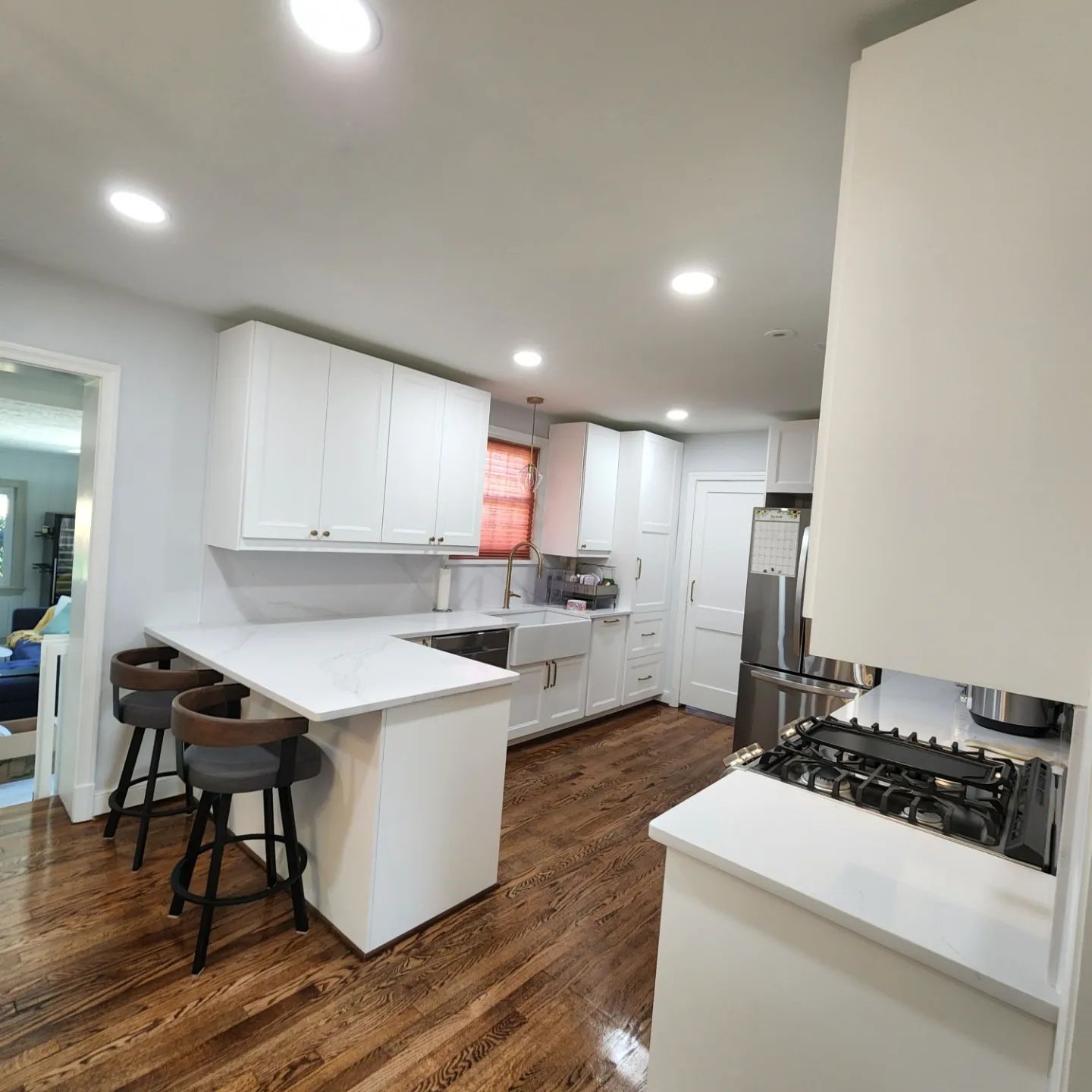 Modern white kitchen with island, stainless appliances, wood floors, and recessed lighting