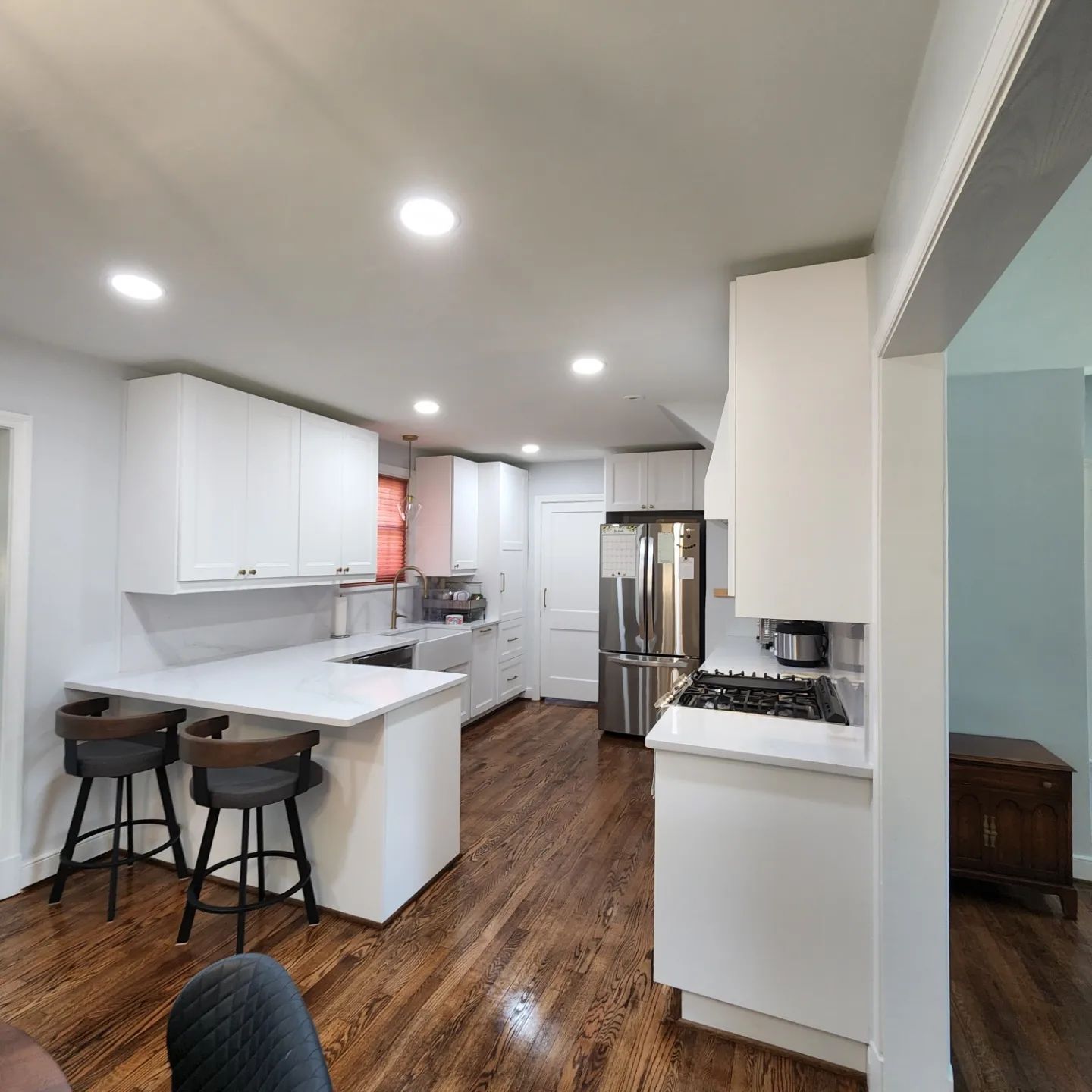 Bright modern kitchen with white cabinets, island stools, stainless steel appliances, and wood floors