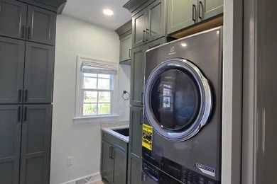 Modern laundry room with gray cabinets, window, sink, and front-loading washer/dryer