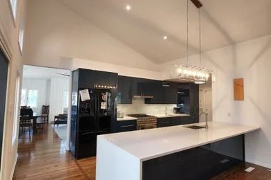 Modern kitchen with black cabinets, white island, hardwood floors, and a dining area in the background