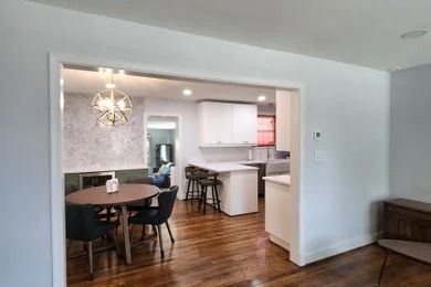 Open-concept dining and kitchen area with wood floors, dark table, white cabinets, and breakfast bar stools