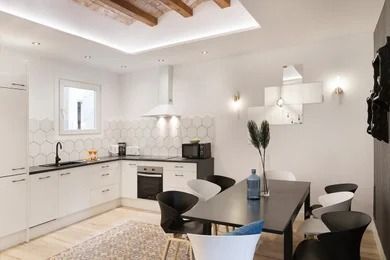 Modern white kitchen and dining area with black chairs, dark table, and exposed wooden ceiling beams