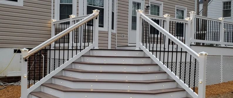 Front steps with white railings leading to a house entrance, with stone siding and porch columns.