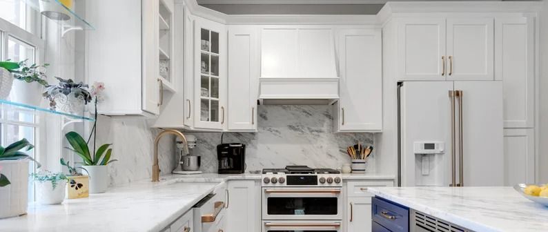 Bright white modern kitchen with marble counters, stainless appliances, and a window over the sink