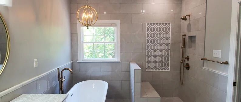 Modern bathroom with tub, walk-in shower, window, and pendant light in gray tile.
