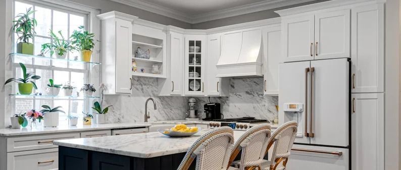 Bright white kitchen with island seating, built-in cabinets, and a window with hanging plants