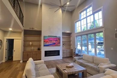 Bright modern living room with high ceiling, fireplace, wall art, beige sofas, and large windows