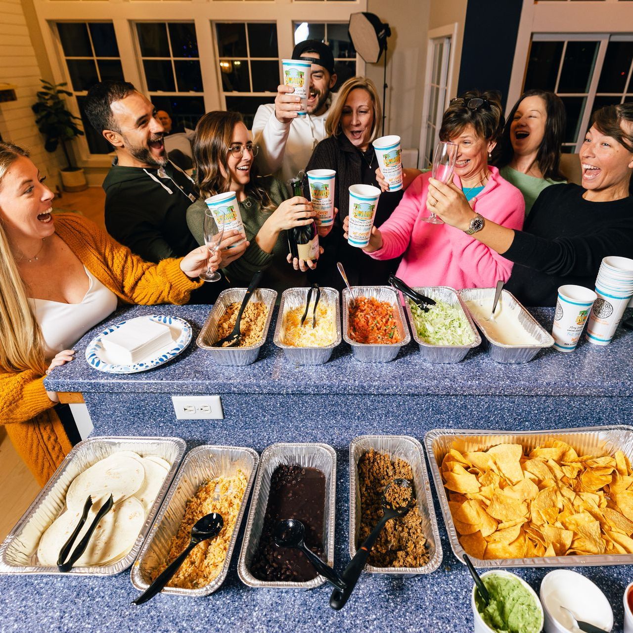 a group of people are standing around a counter with containers of food and drinks including a cup that says ' fiesta '