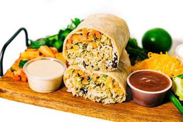 jerk burrito sitting on top of a wooden cutting board next to sauces and vegetables