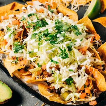 a close up of a plate of nachos with lettuce, sour cream and meat