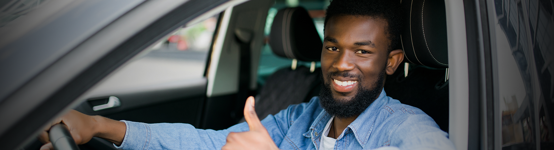 Motorista sorrindo e fazendo sinal de positivo dentro de um carro.