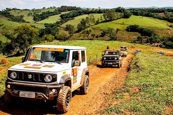 SUVs off-road trafegando por uma trilha de terra lamacenta em meio a colinas verdejantes.