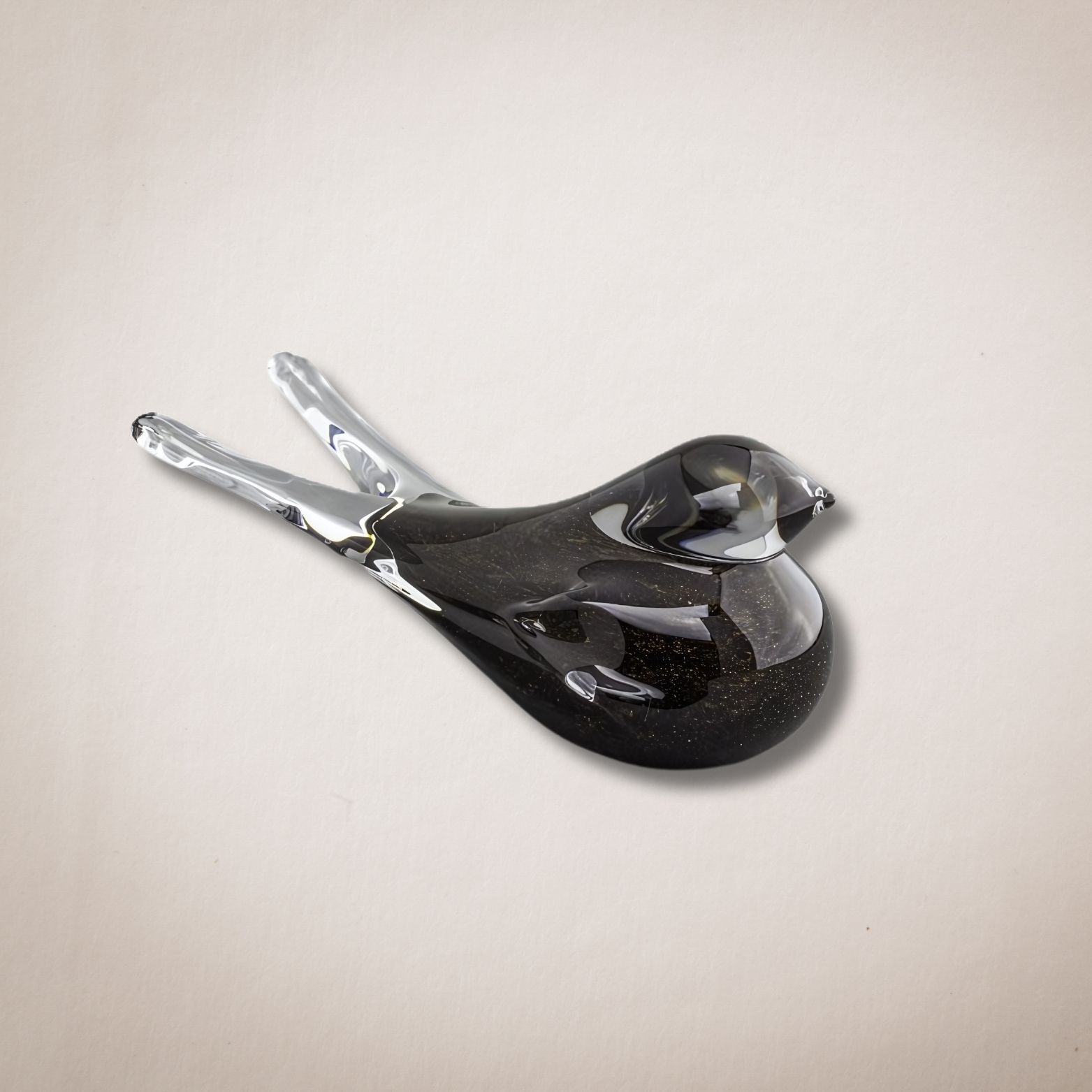 Een zwarte glazen vogel met een zilveren snavel zit op een wit oppervlak