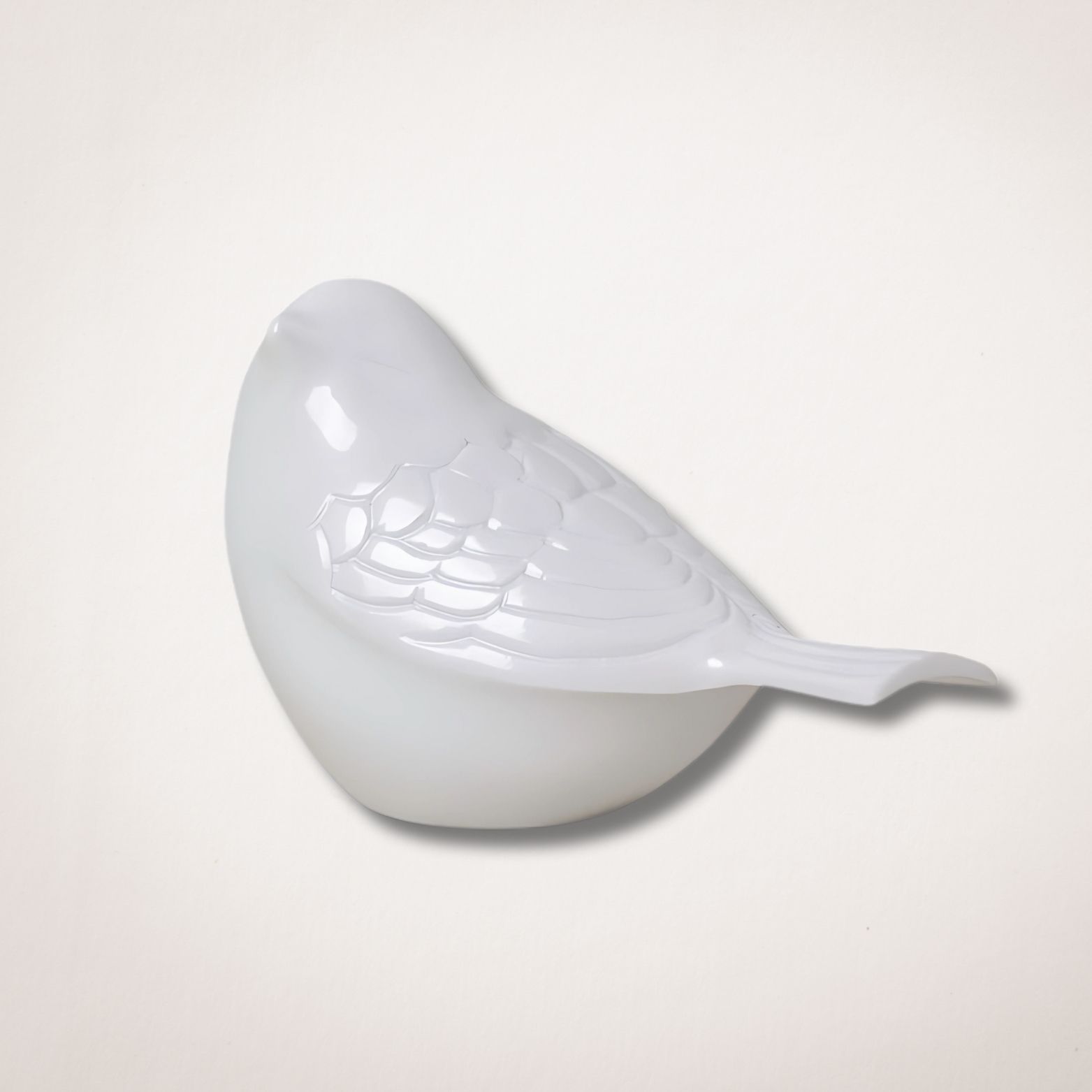 Een wit vogelbeeldje zit op een wit oppervlak.