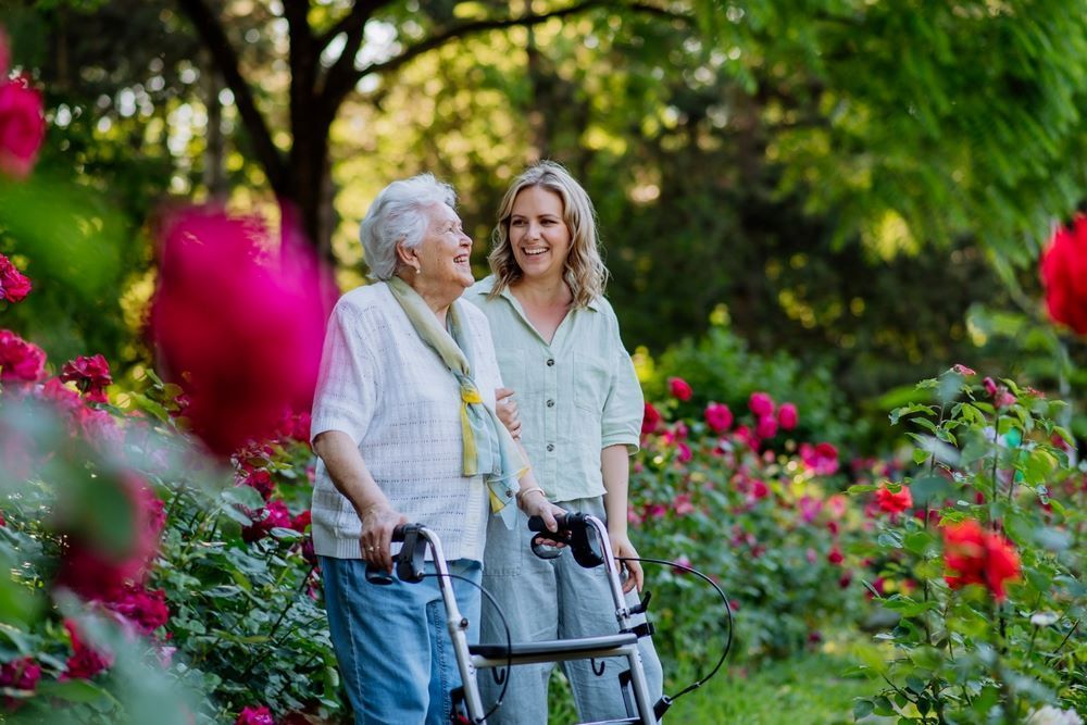 A Woman is Walking With an Elderly Woman With a Walker in a Garden โ Eleos Support Services In Lavington, NSW