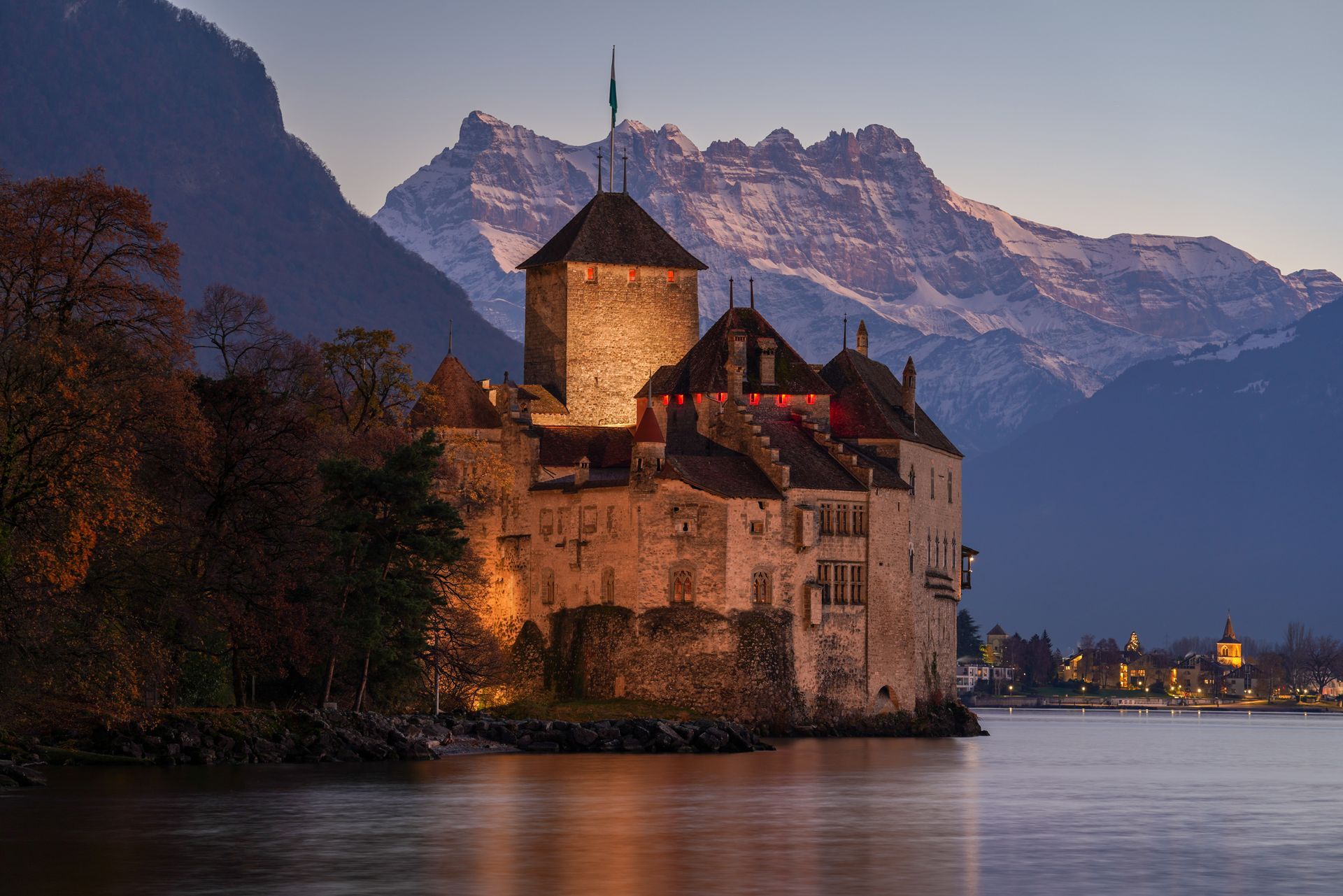 A castle on a small island in the middle of a lake with mountains in the background.