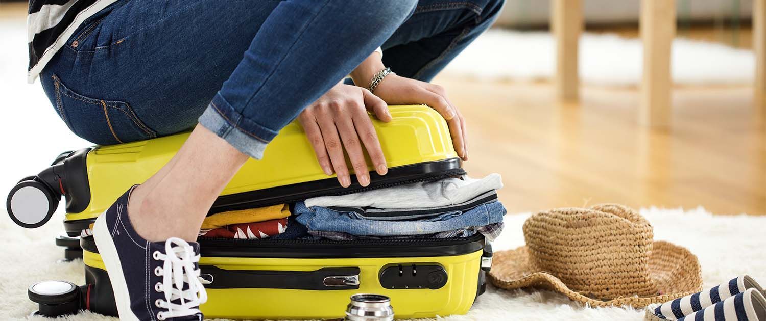 Someone sitting on a yellow suitcase to try close it