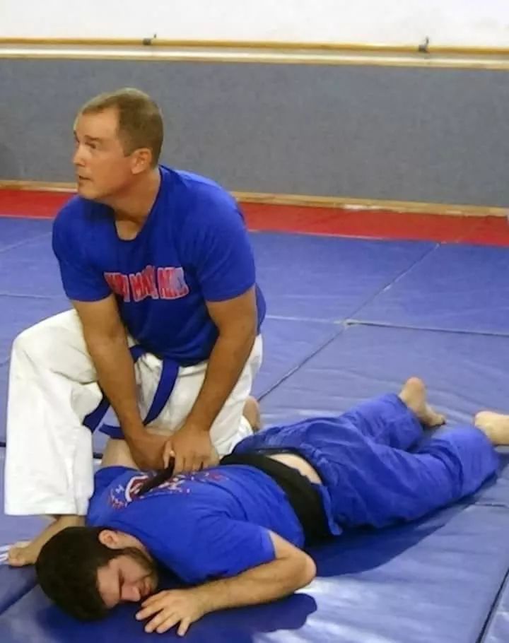 Man performing CPR on a person lying on a blue mat in a gymnasium