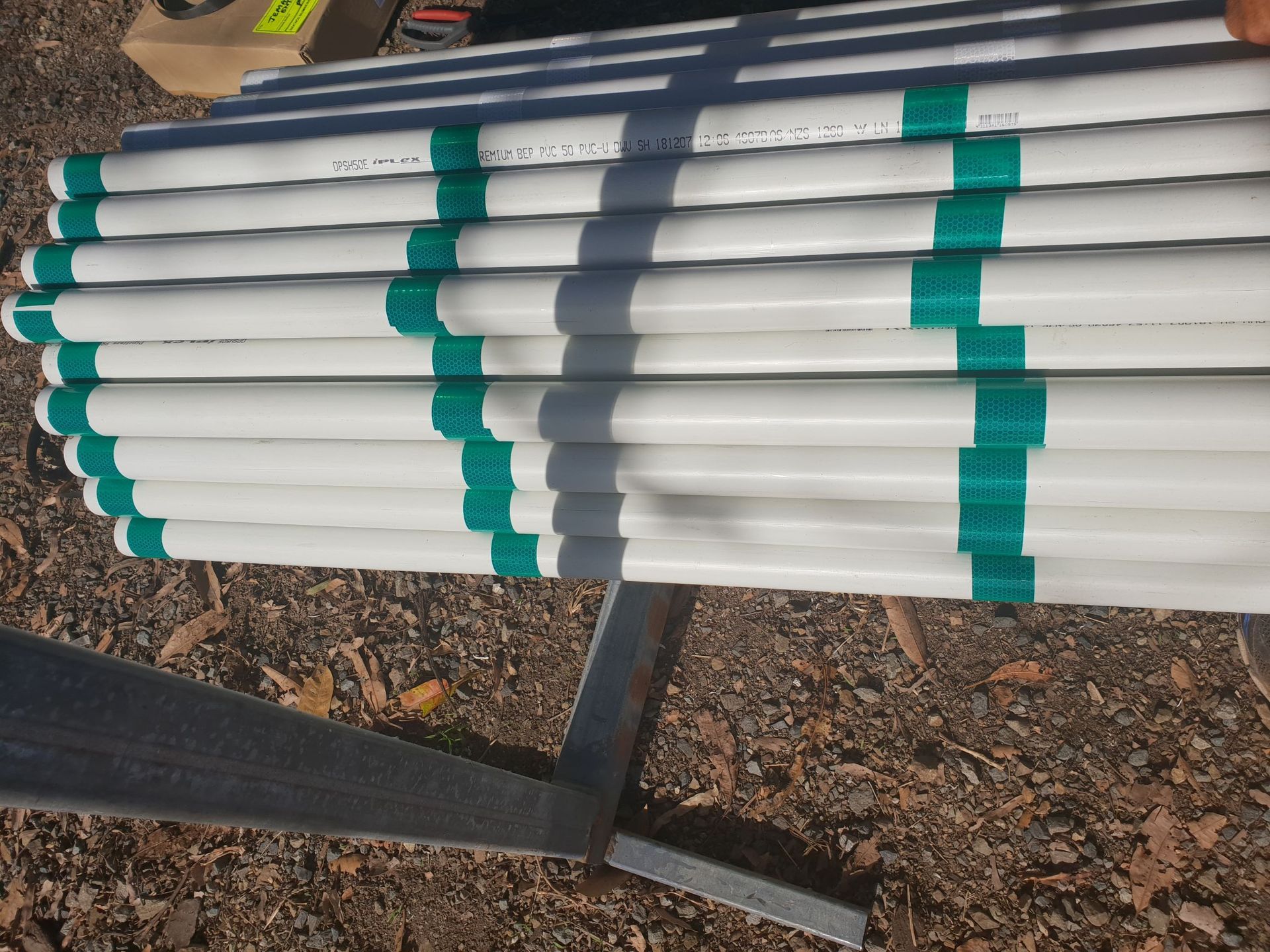 A stack of white PVC pipes with evenly spaced green tape stripes, resting on a metal stand outdoors on gravel — Jemal Enterprises In Finch Hatton, QLD