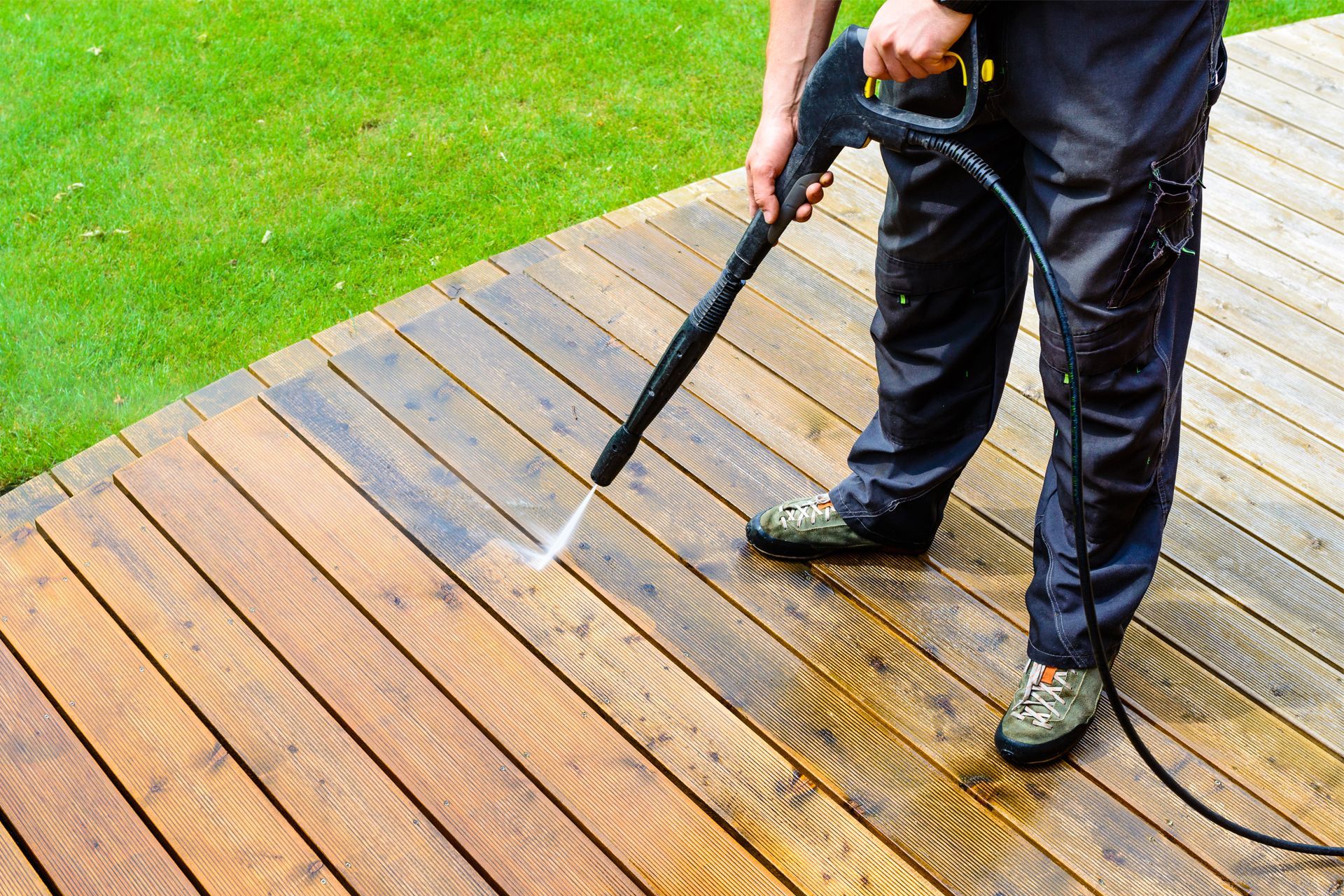 A man is cleaning a wooden deck with a high pressure washer