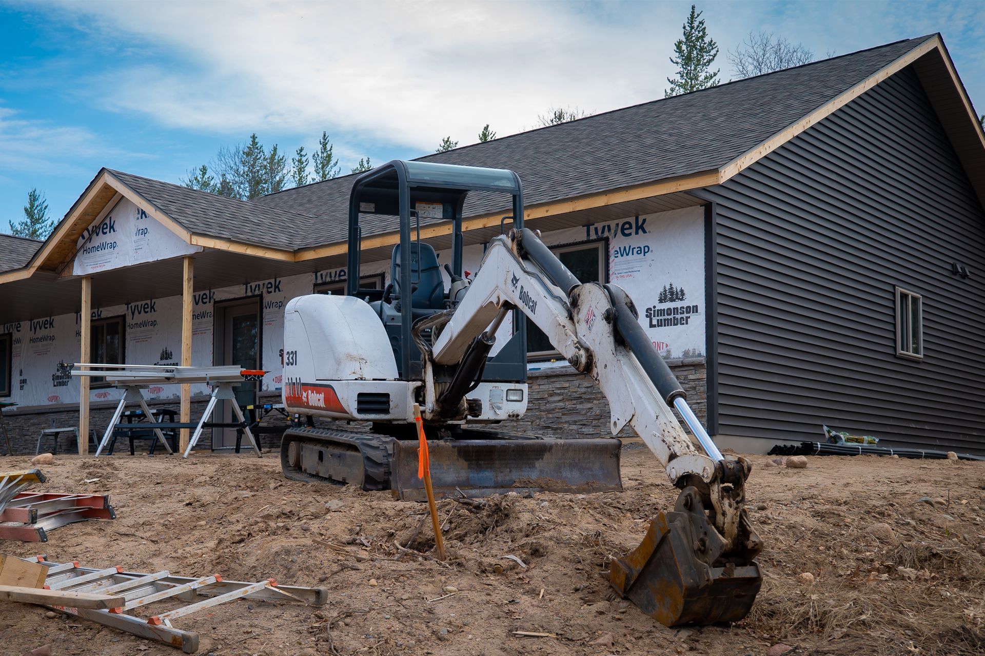 A small excavator is parked in front of a house under construction