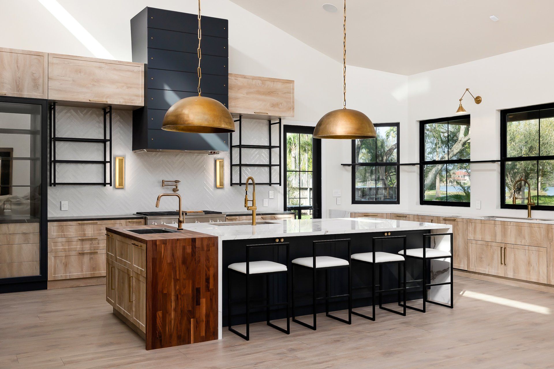 Modern kitchen with large island, brass pendant lights, black-framed windows, and light wood cabinets