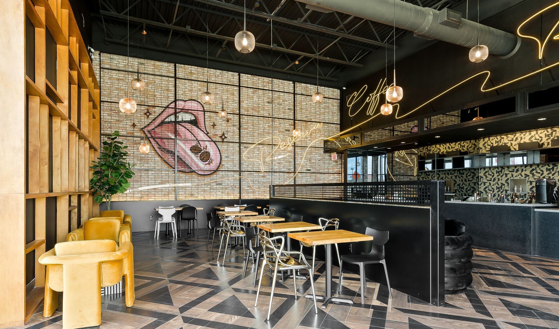 Modern cafe interior with yellow stools, black tables, and geometric tiled floor beneath industrial lighting