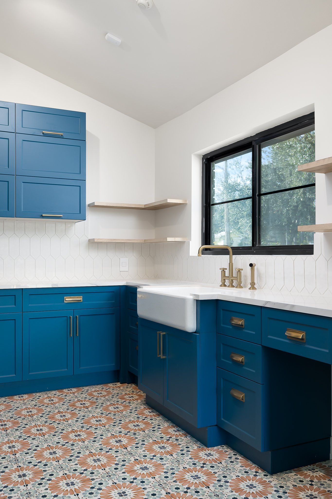 Blue-and-white kitchen with patterned tile floor, black-framed window, and brass cabinet hardware