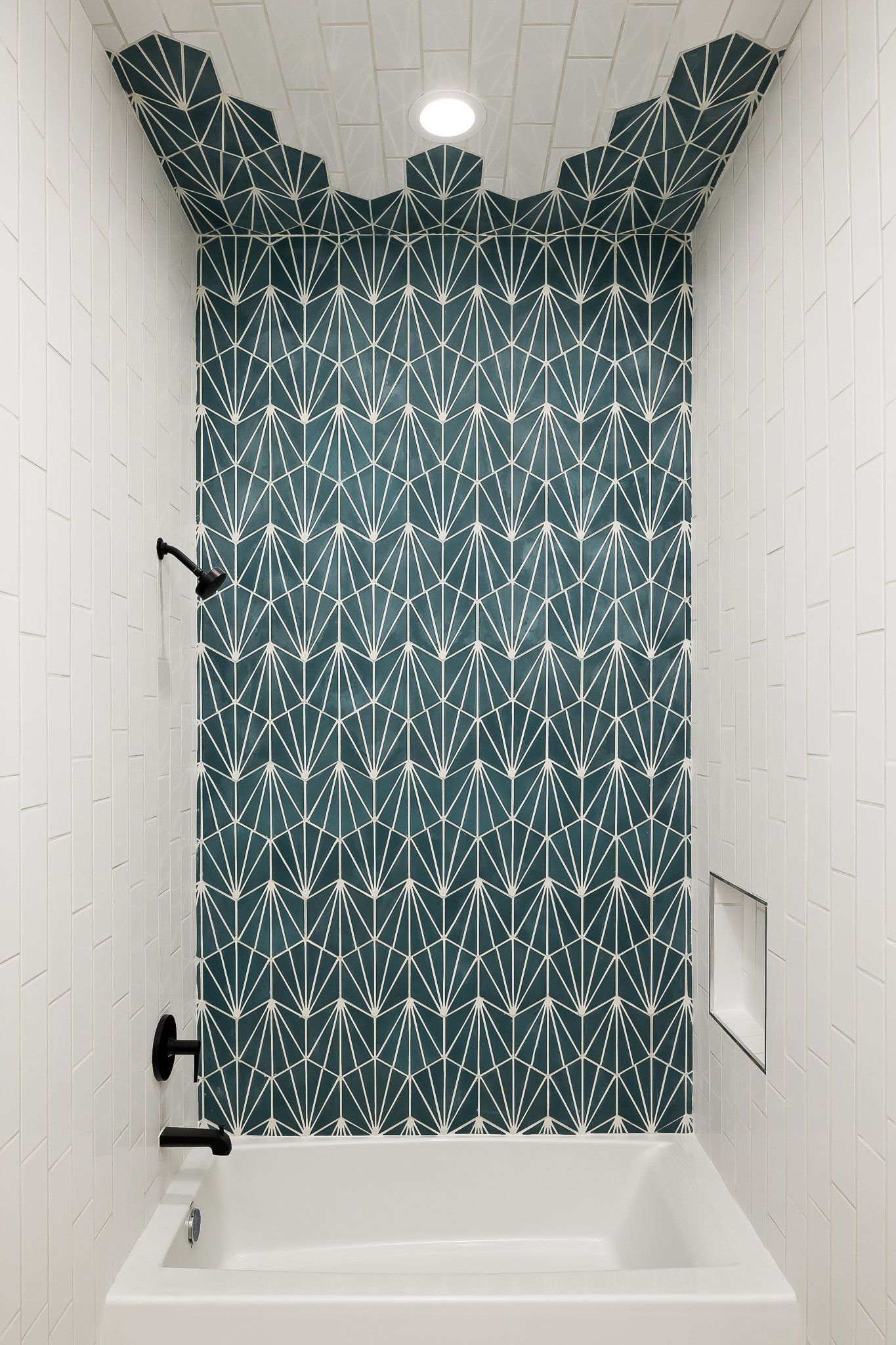 Small tiled shower stall with teal patterned curtain, white walls, bathtub, and mounted shower fixtures