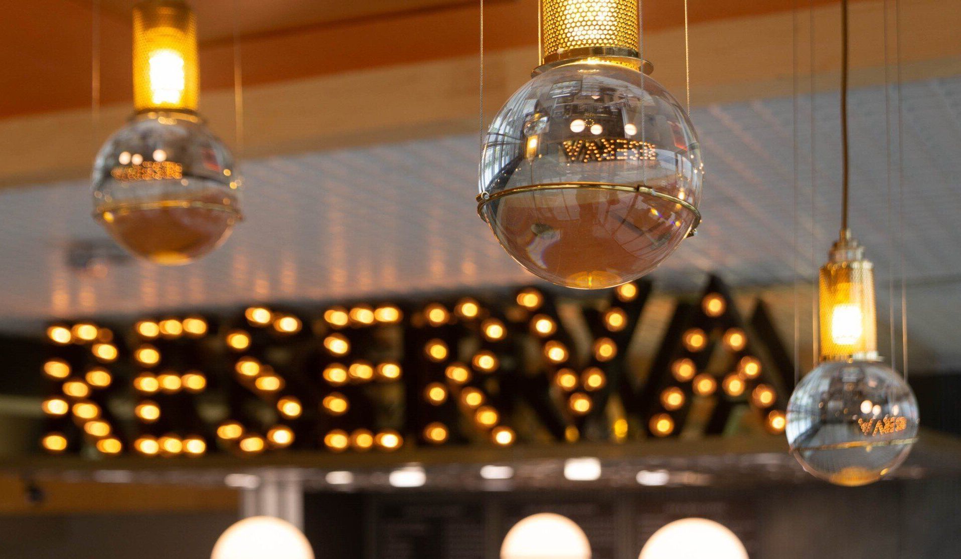 Warm-lit hanging globes above a restaurant sign reading “RESERVA” in glowing dots