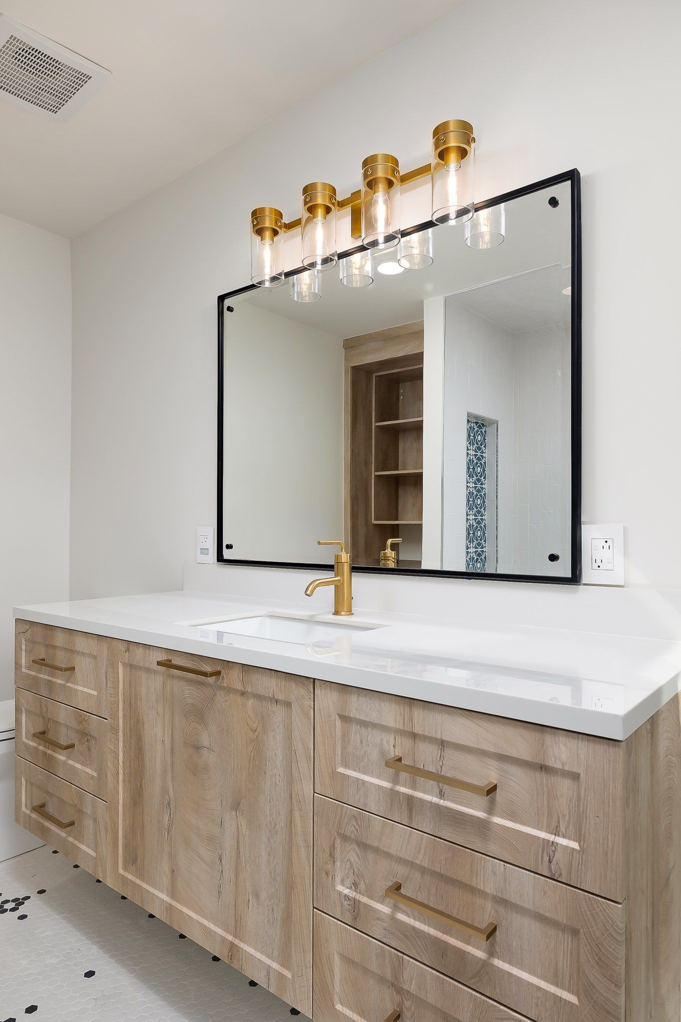 Modern bathroom vanity with white countertop, large mirror, brass sconces, and light wood cabinets