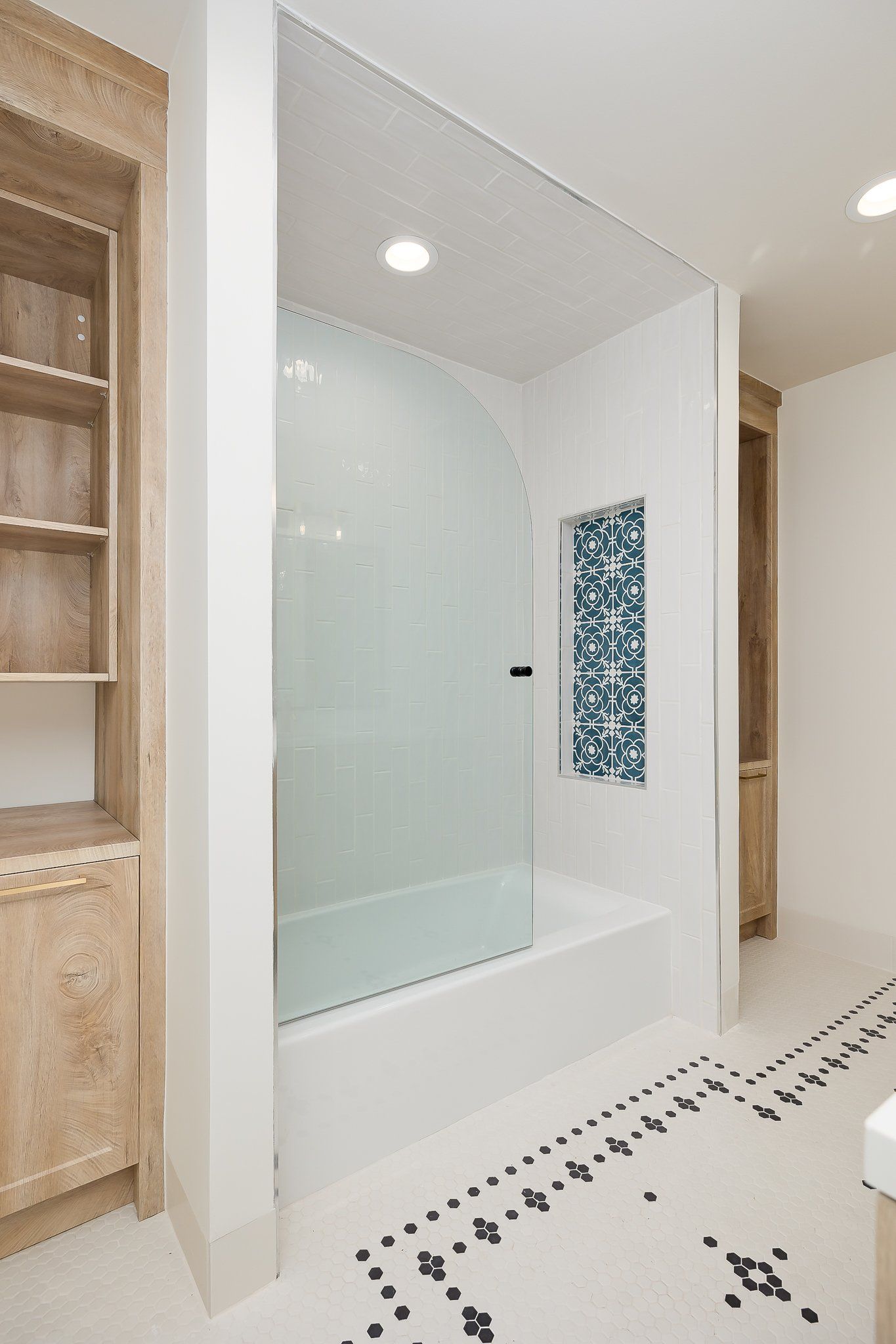 Modern bathroom with glass shower, white tub, and mosaic tile accent wall
