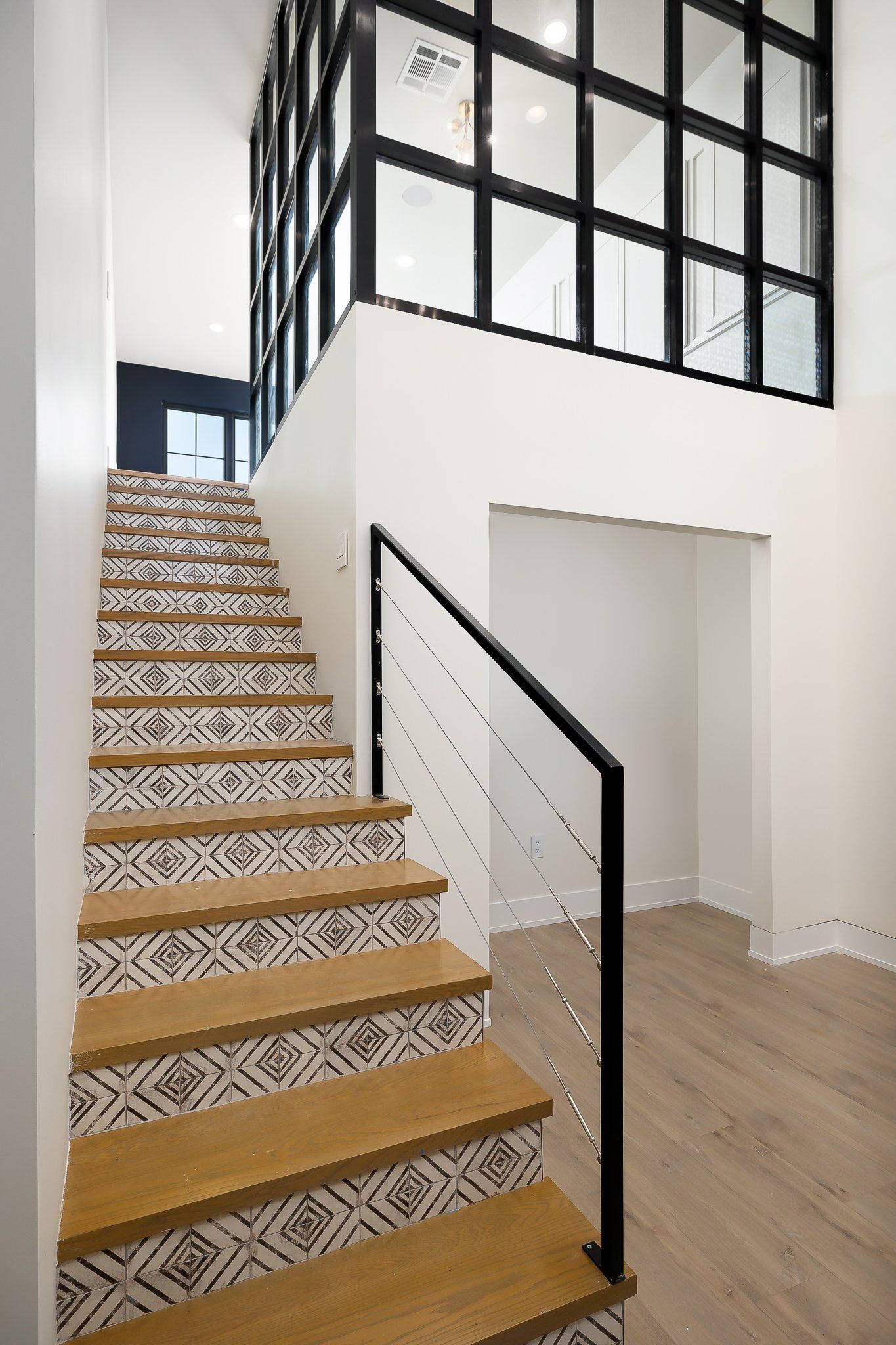 Modern staircase with patterned tiles, black handrail, and white loft-style interior walls.