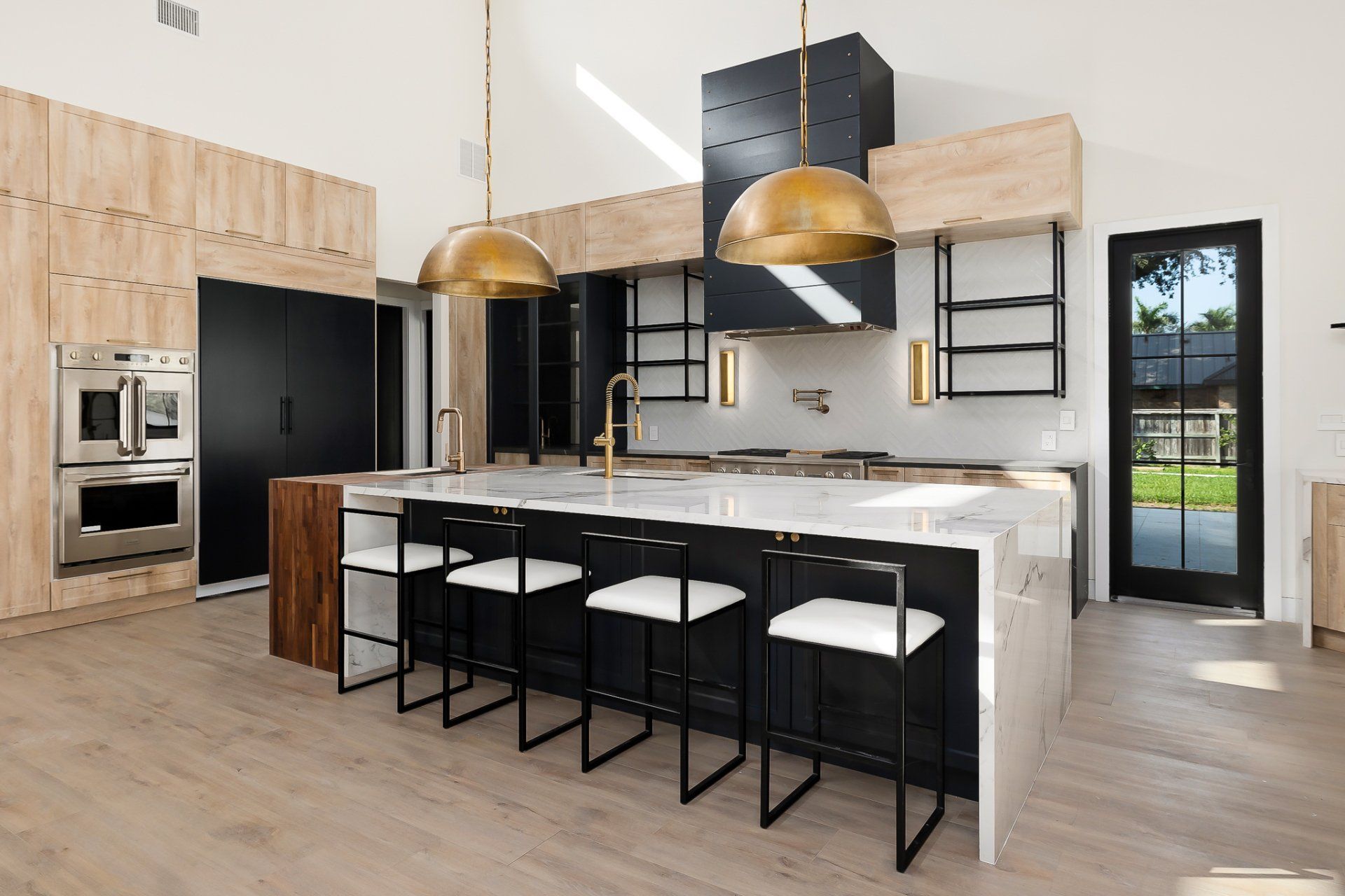 Modern kitchen with black and wood cabinets, marble island, and four bar stools under gold pendant lights