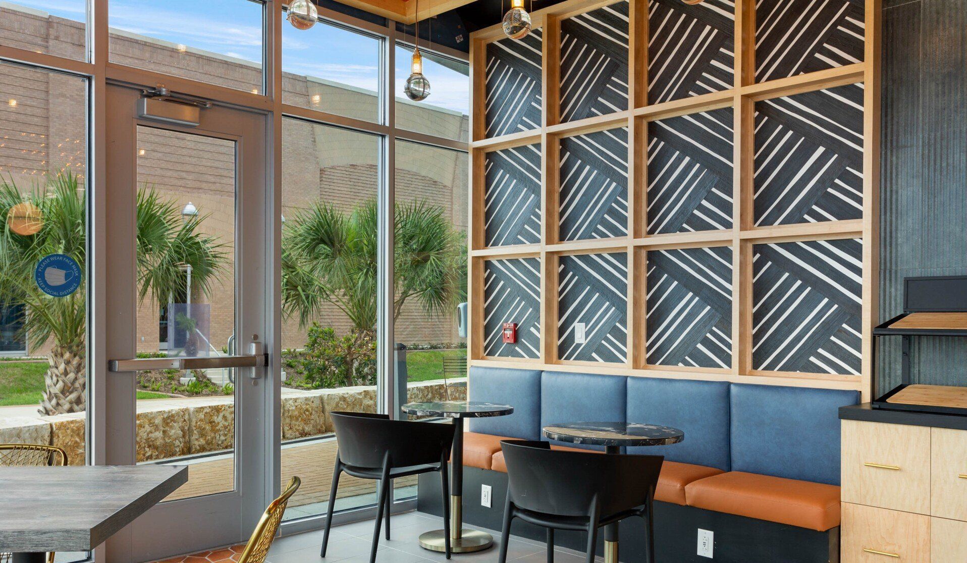 Modern café interior with wooden bench seating, patterned wall panels, and large windows looking outside