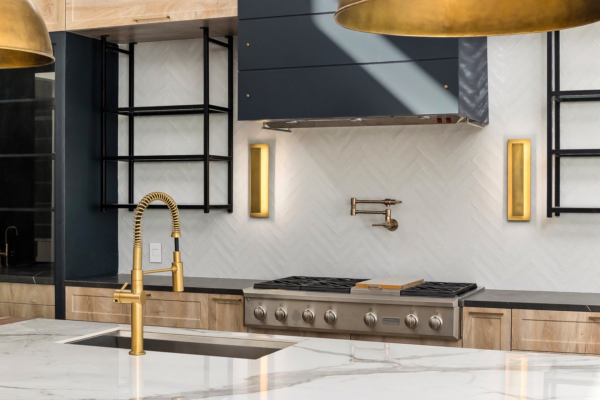 Modern kitchen with white marble island, gold faucet, stainless range, and dark cabinetry