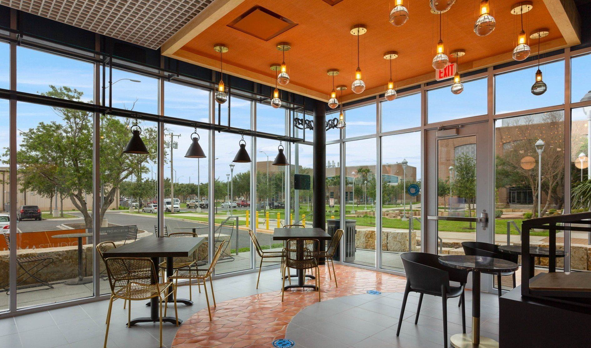 Empty modern cafe with large windows, orange ceiling, hanging lights, and tables facing a green outdoor view