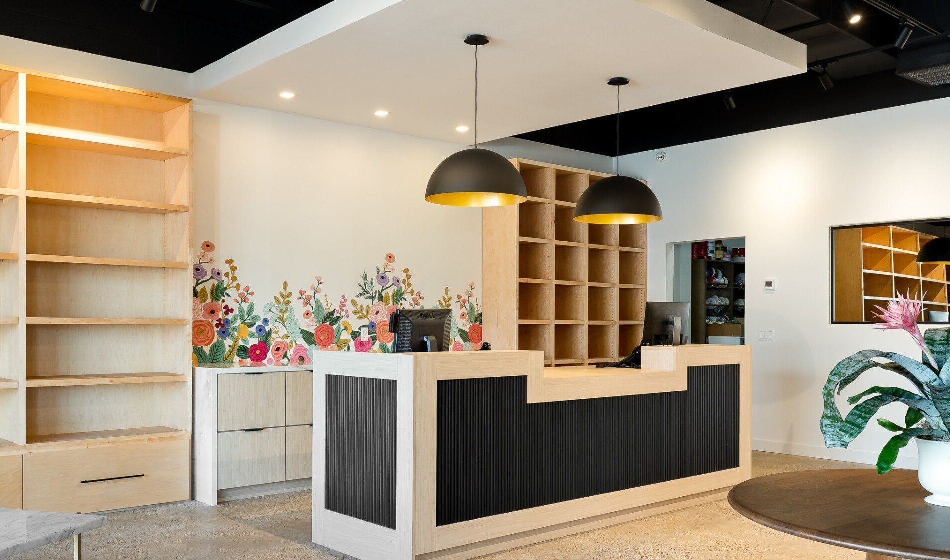Modern hotel lobby with a black-and-white reception desk, pendant lights, and shelving against floral wallpaper
