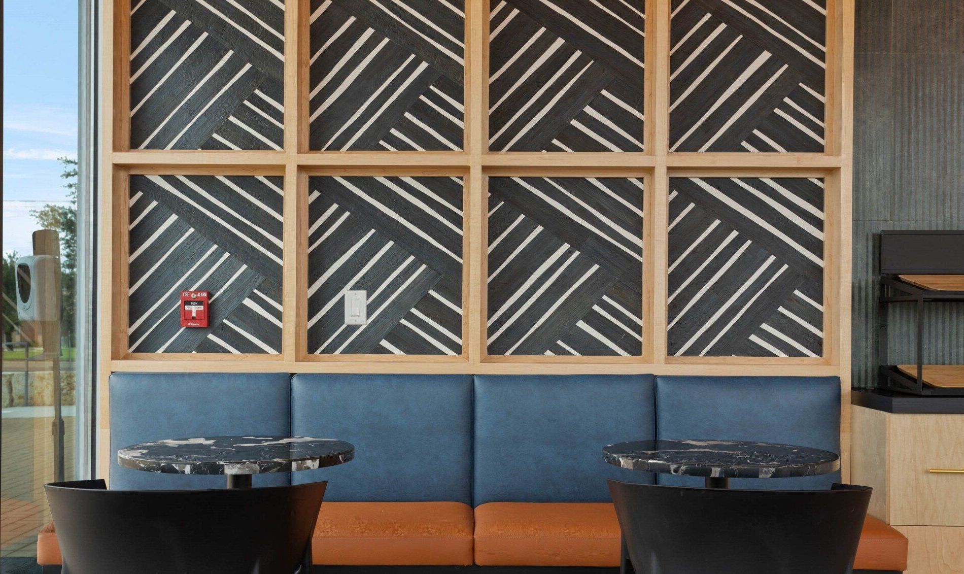 Modern lounge with blue banquette seating, round tables, and a geometric window mural