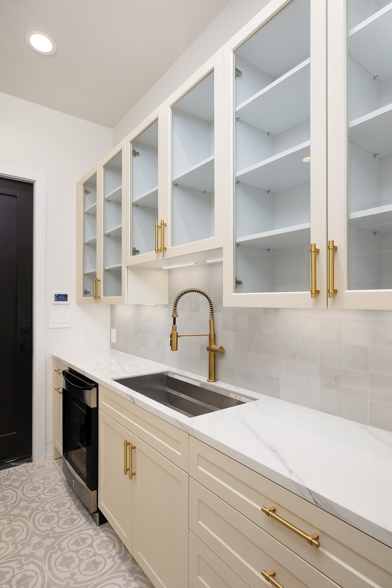 Bright modern kitchen with white cabinets, gold hardware, and a stainless sink along a narrow counter.